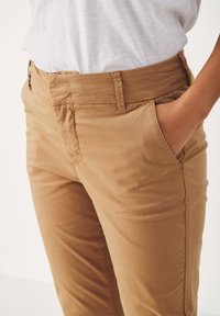Light brown cotton trousers with a smooth texture, featuring side pockets and a flat front waistband, shown against a neutral background.