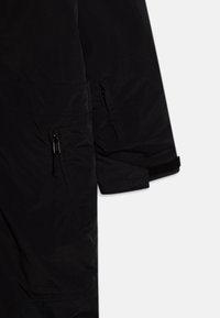 Melna virsdrēbe ar rāvējslēdzēja kabatu, teksturētu audumu un Velcro akcents pie piedurknēm. Elegants, minimālistisks dizains.