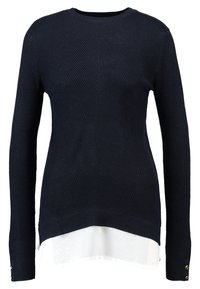 Mörkblå stickad tröja med långa ärmar, som har en texturerad design och en lager på lager vit nederkant. Gula knappar pryder ärmkanterna.