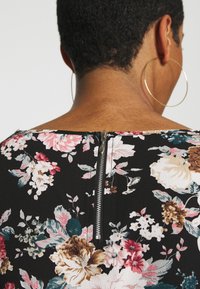 Sort blomsterkjole med tekstureret stof, store pink og hvide blomster samt en metallynlås i ryggen.