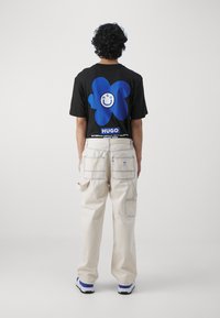 Camiseta negra con un gran gráfico de una flor azul en la parte posterior, combinada con pantalones cargo beige con costuras visibles y múltiples bolsillos.