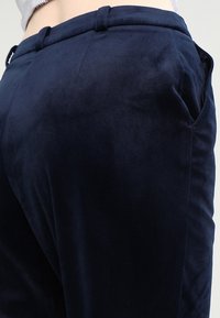 Námořnické modré, měkké zamškové kalhoty s hladkým povrchem, s dobře padnoucím střihem, bočními kapsami a poutky na opasek v pase.