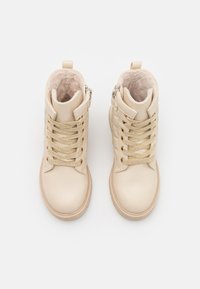Botines beige con cordones dorados, material sintético suave, interior acolchado y cremallera lateral. Punta redondeada y suela plana de goma.