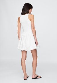 Biele bavlnené šaty bez rukávov s priliehavým živôtikom a rozšírenou, objemnou sukňou, s nariasenou textúrou a dĺžkou nad kolená.