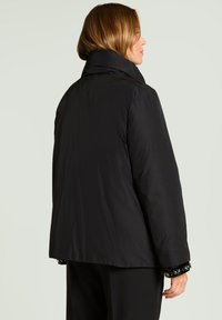 Chaqueta acolchada negra con cuello alto, con una textura suave y un ligero brillo, entallada, con mangas raglán y un ajuste holgado.