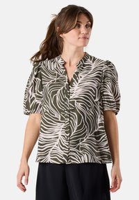 Short-sleeve blouse in olive green with a white leaf pattern, featuring a button closure and a relaxed fit with pleated sleeves.