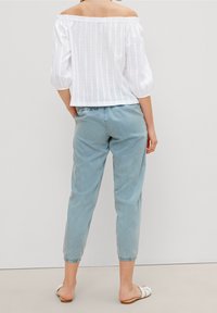 Top bianco, off-shoulder, con texture e maniche a palloncino abbinato a pantaloni azzurro chiaro, a gamba tapered, lunghezza caviglia, e sandali slide bianchi.