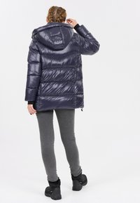 Marinblå pufferjacka med huva, med en glansig finish, horisontell quiltad mönster och justerbara dragsko vid nederkant.