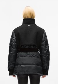 Geacă puf neagră cu o secțiune superioară din lână cropped, guler înalt și talie elastică. Prezintă o textură netedă și lucioasă pe mâneci.