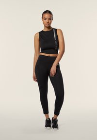 Top corto atletico nero con logo e striscia riflettente, abbinato a leggings neri. Entrambi realizzati in tessuto elasticizzato, design aderente, texture liscia.