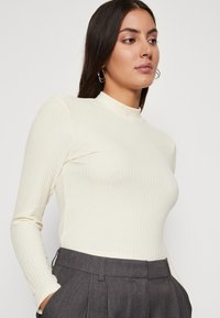 Kremasti rebrasti dugi rukav s visokom ovratnikom, sa slim fit krojem i mekanom teksturom, uparen sivoj krojenim hlačama.