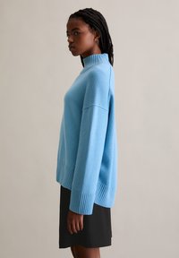 Lichtblauwe trui met hoge kraag, ribgebreide mouwen en zoom, met een losse fit en een zachte, gestructureerde brei.