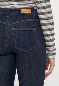 Σκούρες μπλε τζιν παντελόνες σε στενή γραμμή, με πορτοκαλί ραφές, δερμάτινη ένδειξη μάρκας στη μέση και σχέδιο πίσω τσέπης.