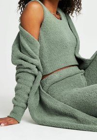 Set da lounge verde con texture realizzato in morbido tessuto, composto da un top senza maniche e un cardigan drappeggiato, con una vestibilità rilassata e un design minimalista.