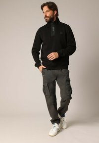 Zwarte zip-up sweatshirt met een gestructureerd paneel bij de nek, gecombineerd met donkere cargobroeken met meerdere zakken en een relaxte pasvorm.