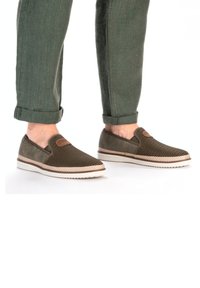 Scarpe slip-on con tomaia in rete intrecciata di colore verde scuro, con dettagli in suede marrone e suola in gomma a contrasto. Bordo testurizzato attorno alla suola.