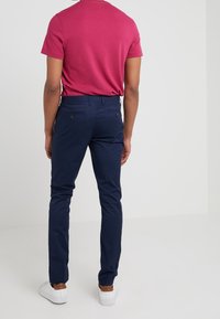 Herrar passande rosa T-shirt i kombination med marinblå byxor. Byxorna har en slät yta, bakfickor med knappar och en avsmalnande design. Vita sneakers.