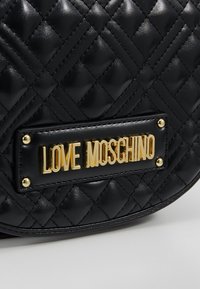 Černá prošívaná taška z umělé kůže s kulatým tvarem a zlatým logem "LOVE MOSCHINO". Má prošitý diamantový vzor a kovové detaily.