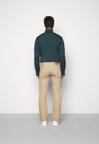 Dark green knitted sweater with a high collar, paired with beige straight-leg pants and white sneakers, viewed from the back.