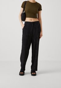 Černé kalhoty s vzorem a velkými textovými grafikami, doplněné dobře padnoucím olivově zeleným tričkem s krátkým rukávem a černými platformovými sandály.