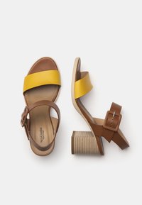 Sandalias de plataforma de cuero marrón con una amplia banda amarilla, que cuentan con una correa en el tobillo con hebilla y un tacón cuña texturizado.