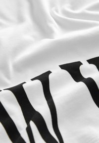 Nahaufnahme von weißem Stoff mit schwarzen teilweise bedruckten Buchstaben, die die Textur und Falten des Gewebes zeigen.