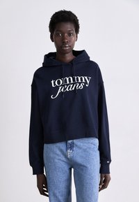 Hoodie cropped blu navy in cotone, con stampa bianca del logo "tommy jeans" sul davanti e cordini sul cappuccio.