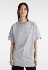 T-shirt en coton gris avec un col rond, des manches courtes et un logo noir sur la poitrine. Présente une coupe décontractée et une texture douce.