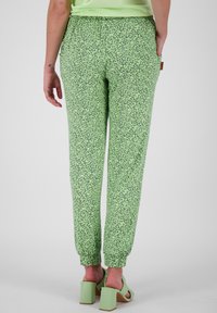 Pantaloni jogger cu imprimeu verde, cu manșete elastice și talie cu șnur; prezintă mici modele florale albe și buzunare laterale.