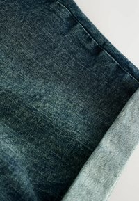 Denim tkanina s tamnoplavim pranjem i svjetloplavim naglascima na rubu. Tekstura je glatka s blagim izblijeđenjem.