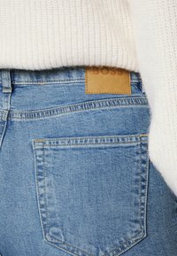 Modré denimové džíny s koženou visačkou s nápisem "BOSS", s texturovanou tkaninou, šitými švy a zadní kapsou.