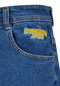 Denim-Jeans in Mittelblau mit sichtbaren Nähten. Verfügt über eine Patttasche und ein gesticktes "homeboy x-tra"-Logo in Orange und Blau.