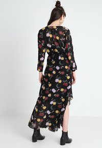 Czarna maxi sukienka w kwiaty z długimi rękawami, lekkim materiałem, kolorowymi wzorami kwiatowymi i asymetrycznym dołem, zestawiona z czarnymi botkami za kostkę.