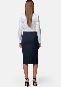 Granatowa spódnica ołówkowa uszyta z dopasowanego materiału, z rozcięciem z tyłu i ukrytym suwakiem. Połączona z białą satynową bluzką z długim rękawem oraz czarnymi szpilkami.