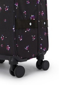 Svart resväska med hjul och ett blommönster i lila, blått och vitt. Har lätt rullande hjul och en textilstruktur. Fastspänd med ett band.