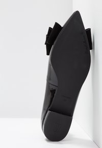 Chaussure à talon aigu en cuir verni noir avec un bout pointu et un accent en nœud texturé noir à l'arrière. Semelle plate avec les détails du fabricant.