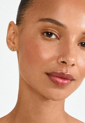 Kuldne südamekujulise naastuga kõrvarõngas vasakul kõrvakul, sile pind, väike suurus, kantud lihtsa ninaringi ja loomuliku nahatekstuuri kõrval.