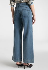 Jeans wide-leg blu chiaro con vita alta, due tasche posteriori e orlo con risvolto. Il tessuto presenta una superficie liscia e leggermente usurata.