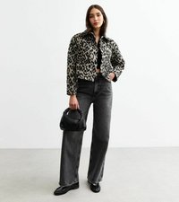 Chaqueta recortada de estampado de leopardo en tela suave, pantalones vaqueros anchos de talle alto negros, bolso negro y bailarinas a juego sobre un suelo liso.