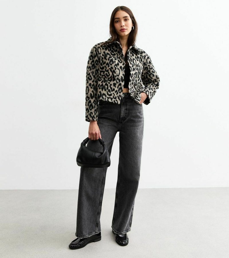 Chaqueta recortada de estampado de leopardo en tela suave, pantalones vaqueros anchos de talle alto negros, bolso negro y bailarinas a juego sobre un suelo liso.