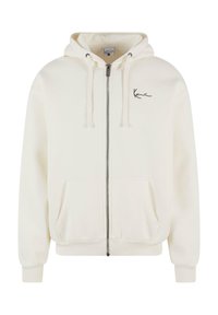 Sudadera blanca con cremallera y capucha con cordón, bolsillos frontales, puños acanalados y un logo negro en el lado izquierdo del pecho. Textura de tela suave.