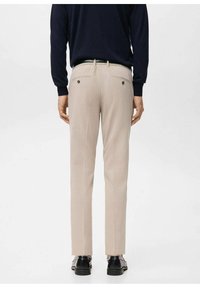 Pantalones beige de corte sastre, con frente plano, dos bolsillos traseros y textura suave. Combinados con zapatos negros.