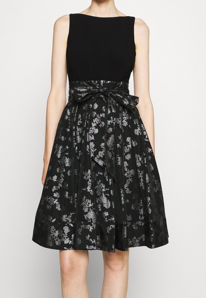 Black dress with a fitted bodice, A-line skirt, and metallic floral patterns. Comes with a matching bow at the waist and a smooth texture.