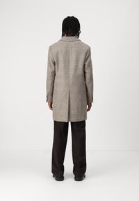 Grå plaid uldfrakke med spids krave, enkelt ventil og manchetter med fire knapper, parret med mørke bukser. Enkel, struktureret design.