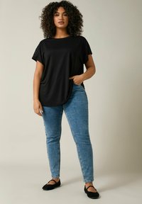 T-shirt nera a taglio rilassato con maniche corte, caratterizzata da dettagli in pizzo sulle maniche. Abbinata a jeans skinny azzurri e ballerine nere.