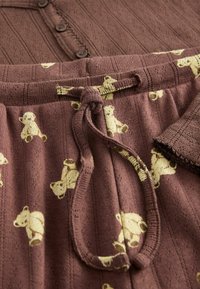 Brunt pyjamasset med ribbad textur som har en knäppningsbar överdel och byxor med elastisk midja dekorerade med gula björnmönster.