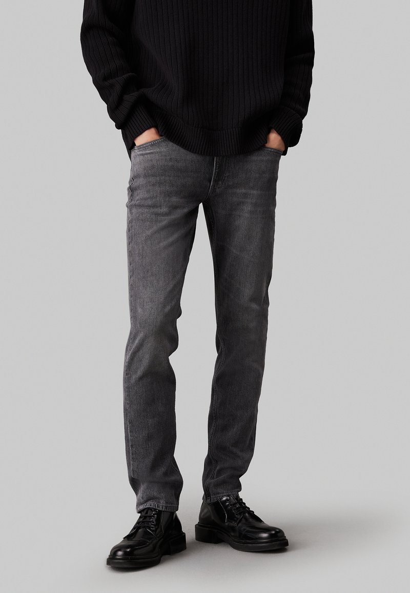 Jeans in denim grigio con una vestibilità slim, caratterizzati da un leggero lavaggio. Abbinati a stivali neri sopra la caviglia e un maglione a coste nero.