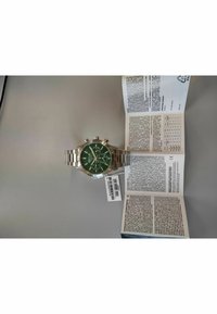 Orologio cronografo in acciaio inossidabile argentato con quadrante verde, tre sottodial, e chiusura pieghevole; manuale e scheda di garanzia visibili accanto.