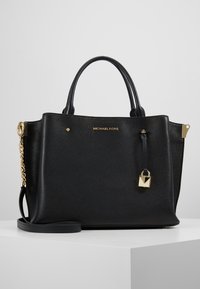 Borsa a mano in pelle nera con finitura texture, hardware dorato, manici superiori, tracolla staccabile e dettaglio con lucchetto. Logo del marchio visibile.