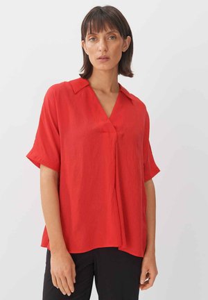 Blusa rossa a maniche corte con colletto e scollatura a V. Tessuto fluido, vestibilità rilassata, caratterizzata da una leggera lucentezza e un dettaglio di piega frontale.